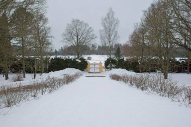 Kapalı beyaz ahşap kapı. Sarı taş çerçeveli. Bulutlu kış havasında ve yerde kar var..