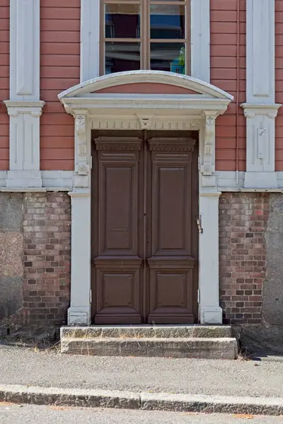 Brown double doors on a wood building with ornamental doorway with stone steps.
