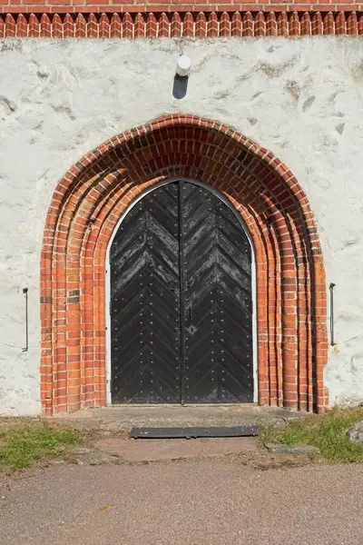 Wooden double doors with arch and a brick frame arch on a old stone building.