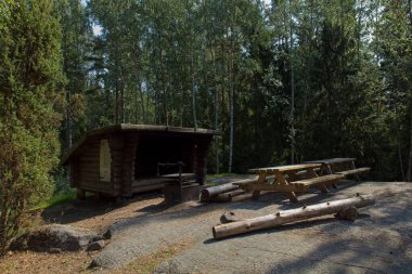 Yazın Kalkinpolttadanpolku doğa yolu boyunca odun barınağı, bank, masa ve kamp ateşi yeri, Sipoo Ulusal Parkı, Finlandiya.