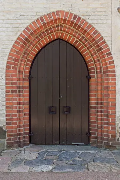 Old wood double doors with red brick arch on a building.