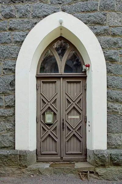Wooden double doors with a arch window with white frame on a stone building.