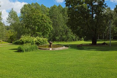 Güneşli yaz havasında parkta akan suyla eski bir taş çeşmenin manzarası..