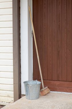 Duvara yaslanmış metal kova ve ahşap fırça temizleme.