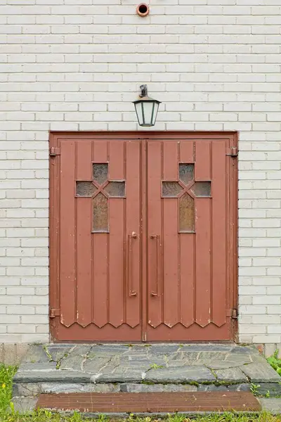 Brown painted wood double doors with glass crosses on a white brcik building with rock step.