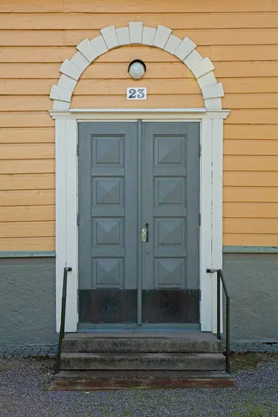 Old decorative grey wood double doors with arch and white frame on a yellow painted wood wall.
