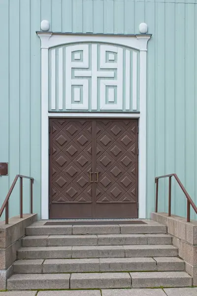 Decorative double doors on a wood building with decoration over door and stone steps.