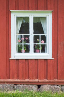 Çiçek saksıları olan kırmızı ahşap bir binanın beyaz çerçeveli penceresi.