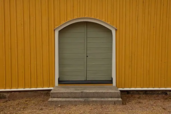 Green wood double doors on a yellow painted wood building.