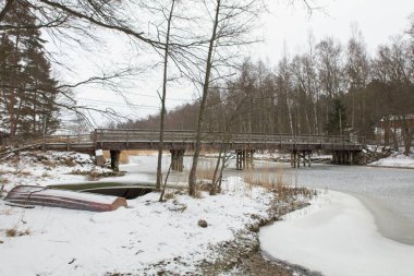 Wooden bridge in cloudy winter weather with sea frozen and snow on the ground, Medvast, Kirkkonummi, Finland. clipart