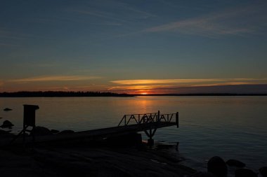 Sonbaharda gökyüzünde bulutlarla birlikte gün batımı, Finlandiya 'nın Espoo, Torra Lovo adasında deniz kıyısında iskele silueti..