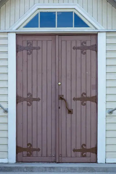 Brown painted old wooden door with decorative iron hinges on wooden building.