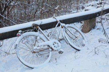 Terk edilmiş bisiklet, kışın korkuluklara yaslanarak karla kaplı..