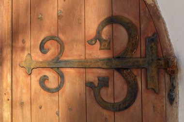 Decorative rustic metal hinge on old wooden door on a stone building. clipart