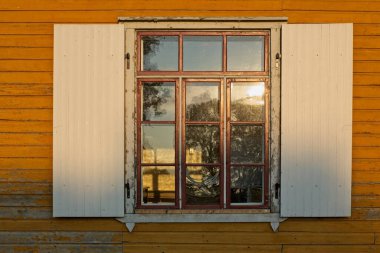 Kahverengi ahşap çerçeve pencereye beyaz dış ahşap panjurlar günbatımında eski sarı ahşap bir bina üzerinde.