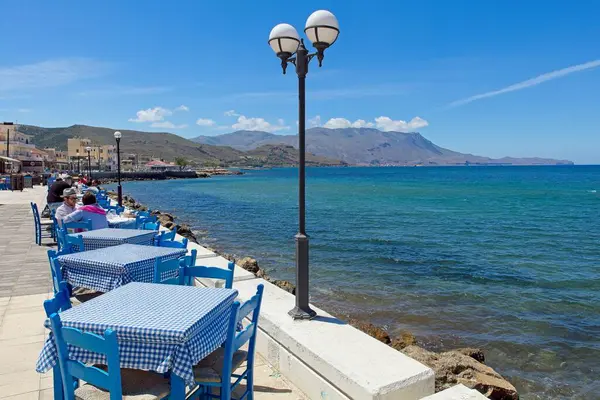 stock image Kissamos, Crete, Greece  May 16, 2019: Restaurant tables beside swashore in Kissamos in spring.