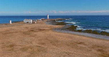 Güneşli yaz mevsiminde 890 nolu yol boyunca Kjolnes Deniz Feneri 'nin hava manzarası Barents Denizi, Varanger Yarımadası, Norveç' ten gelen kayalık sahile vuran dalgalarla birlikte..