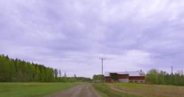 Ylamaa, Finlandiya - 5.16.2023: Çakıl yolunda POV sürmek ve bulutlu bahar havasında bir tarım traktörünün yanından geçmek.