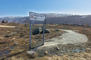 Sign to Norges eldste fjell (Norways oldest mountain) on the Grense Jakobselv road in sunny spring weather, Norway. clipart