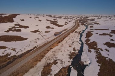 Aerial view of plateau landscape with snow covering the ground and Austertanaveien road 890 in sunny summer weather, Varanger Peninsula, Norway. clipart