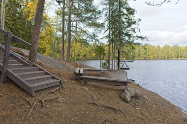 Wooden benches and campfire next to Lapakisto lake on Sammalisto trail in cloudy autumn weather, Lahti, Finland. clipart