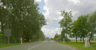 Road E77, Latvia - July 9.2023 : POV view from car driving on the border from Latvia to Lithuania on a asphalt road in summer with clouds in the sky.