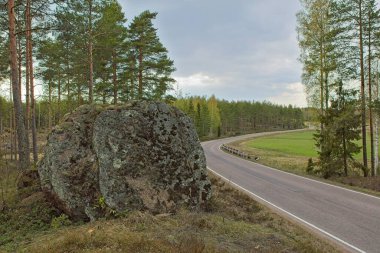 İlkbaharda bulutlu gökyüzü, Rakila, Kymenlaakso, Finlandiya kırsalında asfalt viraj yolu.
