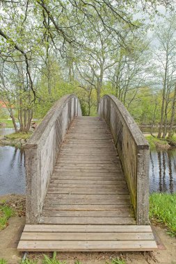Veli Saarinen Parkı 'ndaki tahta köprü Virojoki nehrinde bulutlu bahar havasında bir adaya çıkıyor, Virojoki, Finlandiya.