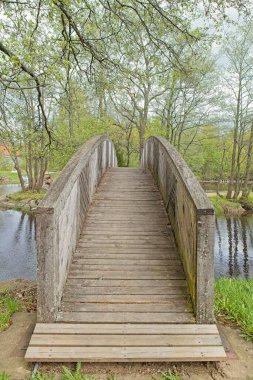 Veli Saarinen Parkı 'ndaki tahta köprü Virojoki nehrinde bulutlu bahar havasında bir adaya çıkıyor, Virojoki, Finlandiya.