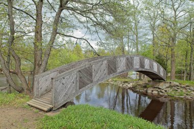 Veli Saarinen Parkı 'ndaki tahta köprü Virojoki nehrinde bulutlu bahar havasında bir adaya çıkıyor, Virojoki, Finlandiya.