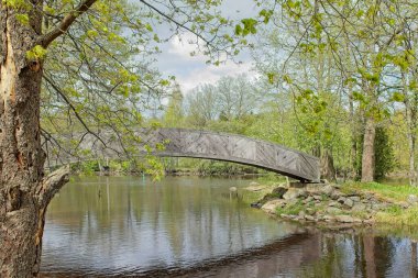 Veli Saarinen Parkı 'ndaki tahta köprü Virojoki nehrinde bulutlu bahar havasında bir adaya çıkıyor, Virojoki, Finlandiya.