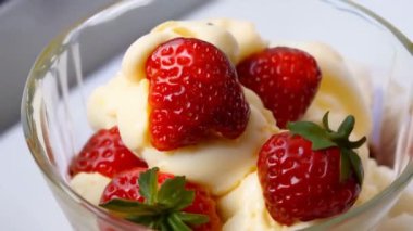 Lezzetli bir kepçe kremalı vanilyalı dondurma taze çilek ve çikolata sosuyla süslenmiş şeffaf bir cam kasede güzelce oturur..