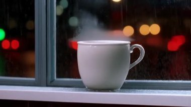Bir fincan kahve pencerenin kenarında durur, pencereden damlayan yağmur damlalarıyla..
