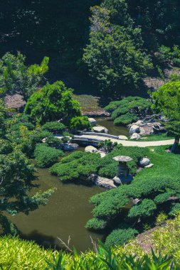 Kavisli bir taş yolu sıcak bir yaz gününde bir Japon bahçesinden geçer. Gölet boyunca kendi yolunu oyarken, yemyeşil yapraklar etrafını sarar. Yüksek kalite fotoğraf