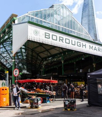 Londra, İngiltere 'de güneşli bir günde arka planda Parça' nın olduğu Borough Market 'in girişi. Kabinler önde görünüyor ve insanlar arka planda alışveriş yapıyor..