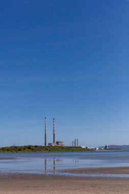 Sandymount beach during low tide with the iconic Poolbeg Chimneys in the background on a bright sunny day. The sky is bright blue against the chimneys. clipart