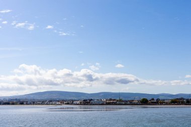 Dublin 'de güneşli bir günde gelgit. Şehrin bir kısmı Dublin Dağları ile kıyı şeridinde yer almaktadır. Gökyüzü birkaç beyaz bulutla mavidir..