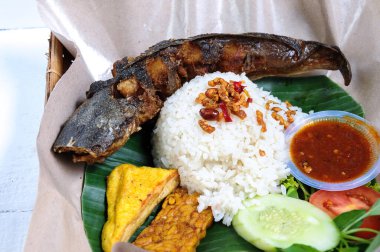 Ikan Lele Goreng 'e kızarmış soya peynirinin yanı sıra sebze ve acı biber sosuyla birlikte beyaz pirinç servis ediliyor.