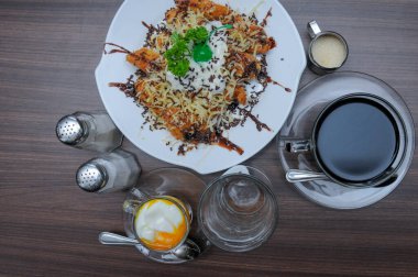 Özel kahvaltı, üzerine peynir ve çikolata serpiştirilmiş muz, yarısı kaynamış yumurta ve sıcak kahve.