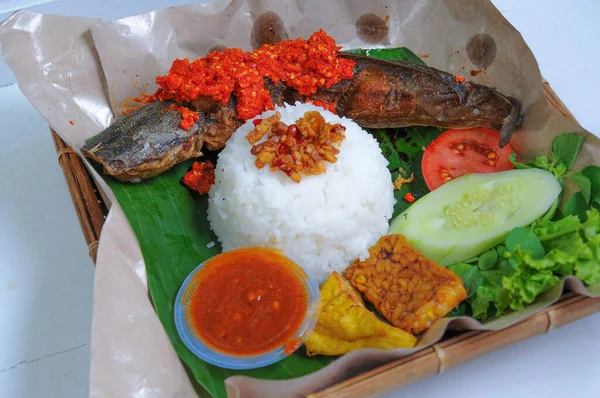 Pecel lele balado with fried catfish and rice covered in scrambled aris tempeh, served with tempeh and fried tofu, as well as chili sauce and vegetables