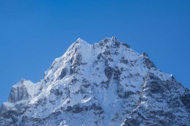 Karla kaplı dağların dingin güzelliğini yansıtan nefes kesici bir manzara. Görkemli zirveler pırıl pırıl parlayan bir kar örtüsüyle bezenmiş, berrak, mavi kış gökyüzüne karşı yükselir..
