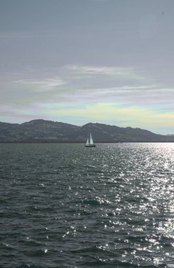 Güneşli bir günde, arka planda dağlar olan bir yat gölde yelken açar..