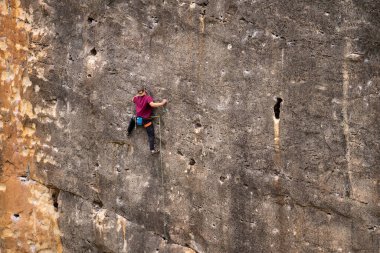 Genç kadın kaya duvarına tırmanıyor.