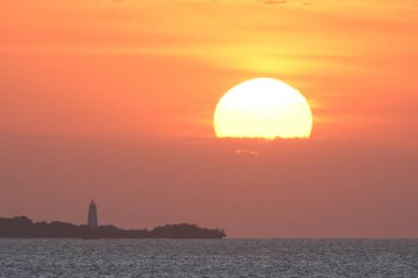 Okyanusun üzerinde bir gün batımı Uzaklarda bir deniz feneri