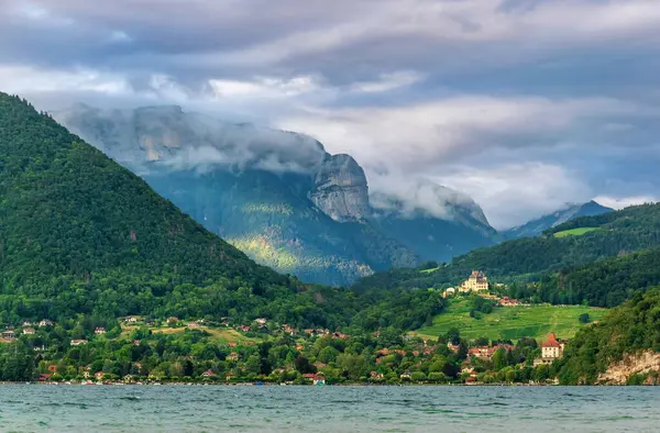 Annecy Gölü 'nün panoramik manzarası. Uzak orman dağları ve bulutlu gökyüzü doğal ışık altında..