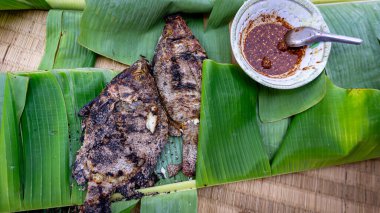 Kırmızı biber soslu ızgara tilapia. Yeşil muz yaprağının üzerinde boş. Kırsal bölgelerde yerel bir yiyecek.