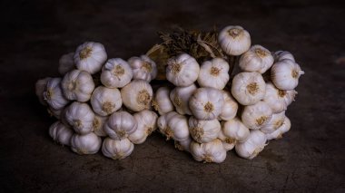 Beyaz sarımsak beton zeminde daireler çiziyor. Işık yukarıdan parlıyor. Her sarımsak yaprağının detaylarını açıkça ortaya koyuyor. Sarımsak karanfillerinin yüzeyi pürüzsüzdür. Yaprağın ucunda hafif bir kırışıklık var. Ve mis kokulu.