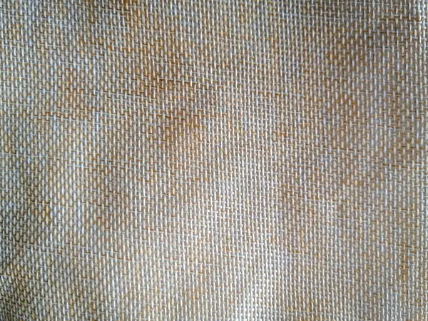 Dokuma kumaşın doğal ve toprak dokusuna sahip yakın plan bir görüntüsü. Kumaş, görünür iplikleri ve hafif parıltısıyla nötr bir bej renktir..