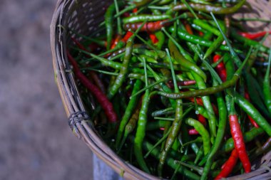 A close-up photo of a basket filled with fresh green and red chili peppers. The peppers are arranged in a pile and have a vibrant color. The basket is made of bamboo and has a rustic appearance. clipart