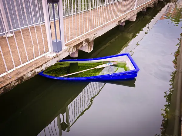 Yansıtıcı sularla çevrili sakin bir kanalda kısmen batan bir kayık. Çürüyen yapı, doğal bir ortamda terk edilme ve nostalji hissi uyandırıyor.